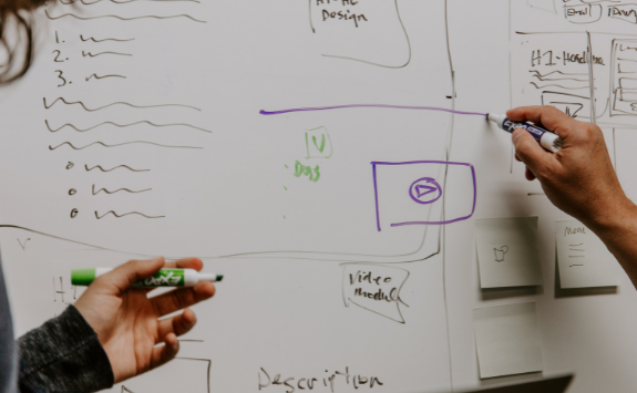 Two people work together on notes on a whiteboard	